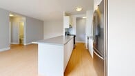 Located at 746 Midland Ave in Toronto's Scarborough area, this 2-bedroom, 1-bathroom unit offers a well-organized single-floor layout finished with light hardwood flooring throughout. The open-concept kitchen and living area form the heart of the space, featuring a galley-style kitchen equipped with stainless steel appliances — including a full-size refrigerator, stove, and dishwasher — white cabinetry, and a peninsula with a grey countertop that doubles as a breakfast bar. The adjacent living room is bright and airy, illuminated by a large picture window with a radiator unit beneath it, providing generous natural light and outdoor views. Both bedrooms are comfortably sized with the same warm hardwood flooring. The primary bedroom includes a sliding door closet, offering practical storage, while the second bedroom features a built-in closet as well. Neutral grey walls run throughout, giving the unit a clean, modern aesthetic. The bathroom is finished with a white tiled tub-and-shower surround and a vanity with integrated sink. A connecting hallway links all rooms efficiently. The unit's bright, neutral palette and functional layout make it a practical and inviting living space.