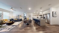 This two-bedroom residence at Avidity in Lutz, Florida showcases a thoughtfully designed open-concept floor plan across a single level. Wood-style flooring flows throughout, connecting the living, dining, and kitchen areas into a cohesive, airy space. The living room features a ceiling fan and large windows with access to a private outdoor area, allowing abundant natural light to fill the room.

The kitchen is a standout feature, outfitted with taupe flat-panel cabinetry, granite countertops, a white subway tile backseat with under-cabinet lighting, and a full suite of stainless steel appliances. A large central island with pendant lighting provides additional counter space and bar seating, ideal for casual dining or entertaining.

Both bedrooms are generously proportioned, each featuring ceiling fans, large windows, and comfortable layouts. Each bedroom is complemented by its own bathroom, finished with granite-topped vanities, wood-style flooring, and direct access to a walk-in closet with built-in shelving and hanging storage. One bathroom includes a soaking tub, while the other features a sleek, functional design. The overall aesthetic throughout the residence is contemporary and cohesive, with a neutral palette accented by modern fixtures and finishes.