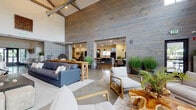 Located at 2000 Day Hill Rd in Windsor, Connecticut, this single-floor amenity space presents a striking blend of industrial and rustic-modern design. The architectural centerpiece is the great room, where dramatically high vaulted ceilings with exposed wooden trusses and ductwork tower above reclaimed wood-clad walls and polished concrete floors, creating a spacious, loft-like atmosphere. Large black-framed glass doors open directly to a covered outdoor patio, flooding the interior with natural light and providing seamless indoor-outdoor connectivity.

The open-plan social area accommodates multiple lounge configurations, featuring plush sectional sofas, accent chairs, and casual high-top seating. A hanging egg chair adds a playful focal point alongside lush potted greenery. Adjacent to the main lounge, a well-appointed kitchen and bar area is anchored by an expansive island with bar seating, pendant lighting, and a retro-style black refrigerator with stone tile backsplash detailing. A full-length shuffleboard table anchors the entertainment zone nearby.

A dedicated golf simulator room offers a high-definition screen and turf hitting mat for year-round play. Quieter lounge nooks with neutral-toned sectionals and natural light provide more intimate gathering options throughout the space.