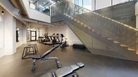 Located at 333 University Avenue in Kingston, Ontario, this contemporary fitness facility offers a well-appointed, open-concept layout across a single floor. The space is defined by its striking double-height ceilings, which flood the interior with natural light through expansive floor-to-ceiling glazing and an upper-level glass mezzanine. Exposed ductwork and industrial-style pendant lighting complement the clean white walls, creating a modern aesthetic that balances function with design.

The flooring throughout consists of durable, dark rubberized fitness matting, providing both safety and performance underfoot. A full-length wall mirror along one side of the space visually expands the room while allowing users to monitor their form during workouts. The cardio zone is well-equipped with multiple treadmills, elliptical trainers, and a stationary bike, arranged to take advantage of the open sightlines. A dedicated free weights area features a tiered dumbbell rack alongside adjustable benches, plyo boxes, and a multi-function cable machine, accommodating a wide range of strength training exercises.

A sleek, glass-panelled staircase adds an architectural focal point, connecting the fitness floor to the upper level. The overall ambiance is bright, clean, and professionally outfitted, making this facility a comprehensive and well-designed space for fitness and training.