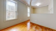 Located at 1601 Main St in the heart of Columbia, SC, this single-floor unit offers an efficient and well-organized layout. Warm, classic hardwood floors run throughout the main living areas, lending a timeless character to the space. The living area is bright and open, benefiting from multiple windows that invite natural light to pour in, illuminating the rich wood tones of the flooring. Decorative crown molding and a textured ceiling add architectural interest and a sense of craftsmanship throughout. A set of classic paneled double doors provides closet storage, enhancing the unit's practicality. The kitchen is thoughtfully equipped with stainless steel appliances, including a full-size refrigerator and electric range, complemented by granite-style countertops, a stainless steel sink, and ample gray upper cabinetry that extends to the ceiling for generous storage. The bathroom features neutral beige walls and clean gray tile flooring, outfitted with a standard toilet and a grab bar, presenting a functional and accessible design. The overall aesthetic is clean and understated, with a warm, neutral color palette throughout that provides a versatile backdrop suitable for a variety of uses.