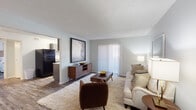 This single-floor residence offers a thoughtfully laid-out living space with a warm, contemporary aesthetic throughout. The living room serves as the heart of the home, featuring wood-look flooring, a textured ceiling, and soft neutral walls that create a calm, inviting atmosphere. A sliding glass door dressed with vertical blinds fills the room with natural light and provides access to the outdoors. The space is anchored by a plush area rug and flows naturally into the kitchen, which is visible through an open pass-through and is equipped with black appliances, including a full-size refrigerator and stove, alongside a functional countertop workspace. The bedroom is a serene retreat, offering generous proportions, a ceiling fan for year-round comfort, a large window with outdoor views, and a wide sliding-door closet with built-in shelving for ample storage. The wood-look flooring carries throughout, lending consistency and warmth to the space. The bathroom is clean and practical, featuring a vanity with a stone-look countertop, grey cabinetry, a well-lit mirror, and a shower-tub combination. Overall, the residence presents a cohesive, modern aesthetic with mid-century inspired touches, balancing comfort and functionality in every room.