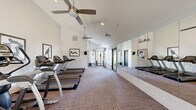 Located at 1700 Paseo Laguna Secoq in Livermore, CA, this fitness center offers a thoughtfully designed workout space on a single floor. The room features soaring vaulted ceilings that lend an airy, open feel, complemented by recessed lighting and dual ceiling fans that maintain a comfortable environment during exercise. Neutral-toned carpet flooring runs throughout the space, while crisp white walls and large windows allow ample natural light to filter in, creating a bright and motivating atmosphere.

A full wall of floor-to-ceiling mirrors lines one side of the room, visually expanding the space and providing exercisers with a clear view of their form. The cardio section is well-appointed with multiple treadmills and elliptical trainers from Matrix, as well as an upright stationary bike. A cable pulley machine anchors the strength training area, while a dedicated functional training zone features a wall-mounted ball rack stocked with medicine balls and stability balls in various sizes. A wall-mounted flat-screen television is positioned for easy viewing during workouts. Motivational athletic silhouette artwork adorns the walls, adding character to the clean, modern aesthetic. Doors at the far end provide access to the outdoors, enhancing ventilation and connectivity to the surrounding grounds.