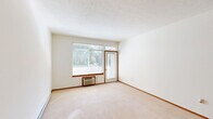 Located in Spokane, WA, this 2-bedroom, 1-bathroom unit offers a well-organized, single-floor layout designed for comfortable everyday living. The living area features neutral-toned carpet, warm wood baseboards, and access to a private balcony through a glass door, with large windows that bring in generous natural light and outdoor views of surrounding greenery. The kitchen is equipped with warm wood cabinetry, a tile backsplash, laminate flooring, an electric range, built-in microwave, refrigerator, and a breakfast bar peninsula that opens to the main living space. Both bedrooms are carpeted and naturally lit, with the primary bedroom offering a comfortable footprint, and the second bedroom featuring a sliding door closet for ample storage. A dedicated hallway connects the rooms, adding to the functional flow of the unit. The bathroom includes a full tub-shower combination, a vanity with a large mirror, and tile countertops. Additional conveniences include two closets, a laundry area, and a utility room. Textured ceilings and consistent warm-toned trim throughout give the unit a cohesive, understated aesthetic well-suited for practical, everyday use.