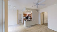 This single-floor residence offers an open and functional layout designed for comfortable everyday living. The main living area features neutral carpeting, a ceiling fan, and track lighting, creating a bright and welcoming atmosphere. A wide arched doorway adds an elegant architectural touch, leading seamlessly between spaces.

The kitchen is the centerpiece of the home, thoughtfully designed with rich warm-toned wood cabinetry, dark granite countertops, and a tile backsplash that adds depth and texture. Stainless steel appliances, including a microwave and range, provide a modern contrast to the classic cabinetry. A peninsula with an integrated sink and pendant lighting overhead defines the kitchen space while maintaining an open connection to the living area, making it ideal for both cooking and casual interaction.

Hallways lead to additional rooms, hinting at a well-organized floor plan with clearly separated living and private zones. The consistent use of neutral tones throughout — from the carpet to the walls — creates a cohesive and versatile interior that is easy to personalize. Overall, the space balances practical design with inviting details, offering a comfortable and well-appointed home environment.