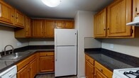 This 1-bedroom, 1-bathroom unit at 278 Main St in West Haven, Connecticut is spread across two floors, offering a practical and comfortable layout. The kitchen is well-appointed with warm honey-toned oak cabinetry, dark granite-style countertops, wood-look vinyl flooring, and a full-size white refrigerator. Ample upper and lower cabinet storage makes the kitchen both functional and efficient. The living area is generously sized, featuring neutral beige carpeting and light-toned walls that create a clean, open atmosphere ready for personalization. A staircase connects the two levels, as seen in the dollhouse view, with the upper floor housing the bedroom and bathroom. The bedroom is comfortably scaled with soft carpeting, neutral walls, and a closet with louvered bifold doors and a built-in rod and shelf for organized storage. The full bathroom is bright and clean, finished with light wood-look flooring, white fixtures, a tub and shower combo with a curved curtain rod, and a white vanity with countertop sink. The overall aesthetic throughout is neutral and move-in ready, offering a straightforward, functional living space in a convenient West Haven location.