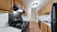 This single-floor residence offers a straightforward and functional layout designed for comfortable everyday living. The kitchen is well-equipped with warm honey-toned wood cabinetry providing generous upper and lower storage, light countertops, a black electric range with overhead ventilation, a dishwasher, and a sink — all set atop durable wood-look flooring that extends throughout the main living areas. A tall pantry-style cabinet adds extra storage capacity alongside the kitchen. The open living and dining area is bright and clean, featuring neutral walls, a tiled ceiling, and wood-look flooring that lends warmth to the space. A second room, which functions as a bedroom or additional living space, benefits from large sliding glass doors fitted with vertical blinds, allowing natural light to filter in and providing access to an outdoor view. The carpeted bedroom offers a quiet retreat with a spacious closet for ample storage. A hallway connects the main living areas to the bathroom, which features a full tub-shower combination. The corridor also includes a security panel and louvered closet doors, adding both convenience and practicality to the home's efficient design.