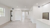 Located at 710 Seventh Street in the heart of Miami Beach, FL, this 2-bedroom, 1-bathroom residence offers a clean, modern aesthetic defined by an all-white palette and thoughtful design throughout. The single-floor layout flows efficiently from room to room, connected by a central hallway.

The kitchen is a standout feature, showcasing high-gloss white cabinetry extending to the ceiling, a white quartz peninsula with an undermount sink and brushed brass faucet, stainless steel appliances including a full-size refrigerator and range, and a built-in microwave. Natural light filters in through a gridded window, enhancing the bright, airy atmosphere.

The living and common areas feature light-toned tile flooring, recessed ceiling lighting, and crisp white walls that give the space an open, uncluttered feel. Louvered bifold closet doors add a subtle textural contrast in the main living area. The primary bedroom is generously proportioned and bathed in natural light from multiple gridded windows overlooking lush greenery. Both bedrooms are fitted with built-in sliding-door closets offering organized shelving and hanging rods.

The bathroom is clean and minimal, featuring recessed lighting, a wall-mounted vanity, and consistent light tile flooring. The overall ambiance is modern, bright, and move-in ready.
