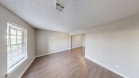 This two-bedroom, one-bathroom two-story home offers a well-organized layout spread across two floors. The main floor houses the combined kitchen and living area, a laundry room, and a connecting hallway. The open living room features warm hardwood-style flooring, a ceiling fan with light fixture, and a large window that fills the space with natural light. A half-wall pass-through connects the living area to the kitchen, which is equipped with white shaker-style cabinetry with black hardware, a double-basin sink with a matte black faucet, white countertops, an under-cabinet range hood, and a skylight-style overhead light fixture. The laundry room is conveniently accessible directly from the kitchen. The upper floor accommodates both bedrooms and the full bathroom. Each bedroom features hardwood-style flooring, neutral wall tones, ceiling fans, and windows with white blinds that invite natural light. The primary bedroom is generously sized with a closet and a window overlooking the exterior. The shared bathroom includes a tub-shower combo with clean white subway tile surround and glass corner shelving. Textured ceilings are present throughout, adding a classic character to the home's overall clean and neutral aesthetic.