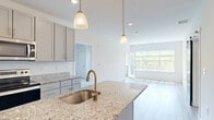 This two-bedroom, two-bathroom residence offers a thoughtfully designed layout spread across two floors, combining modern finishes with a bright, open aesthetic. The kitchen serves as a central highlight, featuring granite countertops, a large center island with a stainless steel sink and brushed gold faucet, gray shaker-style cabinetry extending to the ceiling, and a full suite of stainless steel appliances. Pendant lighting adds a refined touch above the island. The kitchen flows seamlessly into the living room, which is bathed in natural light from expansive windows overlooking lush greenery, with light hardwood-style flooring tying the spaces together. A private balcony accessible from the living area offers serene views of a manicured lawn, mature trees, and a wooden fence line. The primary bedroom is generously sized, with soft carpet flooring, a large window framing outdoor views, and direct access to a spacious walk-in closet equipped with wire shelving. The second bedroom is equally comfortable, also featuring carpet and ample natural light. Both bathrooms are clean and functional, with one including a full tub-shower combination fitted with brushed gold fixtures. A hallway and dedicated closet complete the floor plan, providing practical storage and circulation throughout the home.