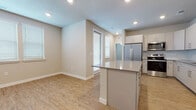 This single-floor unit offers a cohesive, modern design characterized by a neutral color palette, light wood-look flooring, and an abundance of natural light throughout. The kitchen serves as the centerpiece of the open-concept living area, featuring white cabinetry with gold-toned hardware, a subway tile backsplash, quartz-style countertops, and a full suite of stainless steel appliances including a side-by-side refrigerator, range, and microwave. A sizeable central island provides additional prep space and storage, flowing seamlessly into the adjacent living area.

The bedrooms are carpeted in a soft neutral tone and each benefit from multiple windows fitted with horizontal blinds, allowing for controlled natural light. One room features light wood-look flooring and direct access to an exterior door, adding versatility to its use.

Two bathrooms complete the unit. The full bathroom includes a tub-shower combo, wood-look tile flooring, and a vanity with a quartz countertop. The second bathroom features a walk-in shower, a tall linen storage cabinet, an oversized mirror, and a matching vanity—offering a more refined, primary suite aesthetic. A laundry area is also present within the unit.