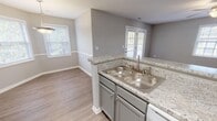 Located at 126 Post Oak Ln in Sanford, NC, this single-story home offers a well-designed, open-concept layout finished with consistent, neutral-toned details throughout. The living area is generously sized, featuring wood-look luxury vinyl flooring, a ceiling fan with integrated lighting, and a textured ceiling. French doors along the rear wall allow natural light to pour in while providing direct access to an outdoor space, enhancing the overall sense of openness.

The kitchen is positioned centrally and defined by a raised peninsula with granite-style countertops, creating a natural separation between the cooking and dining areas. Gray cabinetry, white appliances, and a double-basin sink contribute to a clean, functional aesthetic. An adjacent dining area benefits from natural light through a window and a pendant light fixture overhead.

The bedrooms are comfortable and well-proportioned, each featuring wood-look flooring, ceiling fans or flush-mount lighting, and windows that bring in natural light. The bathrooms are finished with matching granite-style countertops, gray vanity cabinetry, framed mirrors, and brushed nickel fixtures, providing a cohesive look across the home. The overall design is clean, modern, and move-in ready.