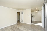 This single-floor residence offers a practical and comfortable layout designed for everyday living. The kitchen is a standout feature, outfitted with crisp white cabinetry accented by dark hardware, granite-look countertops, and durable wood-look flooring. A full suite of appliances — including a black refrigerator, electric range, and over-the-range microwave — ensures the kitchen is move-in ready. Ample upper and lower cabinet storage, along with a single-basin sink illuminated by warm vanity-style lighting, rounds out this functional cooking space. The bathroom is finished with floor-to-ceiling beige tile surrounding a full soaking tub with an overhead handheld shower fixture. A clean white vanity and mirror complete the space, creating a calm, neutral aesthetic. The living area features plush carpeting and is anchored by a wall of sliding glass doors that flood the room with natural light and provide direct access to a private outdoor patio. The patio is enclosed by fencing and lush greenery, offering a sense of seclusion. Throughout the residence, a consistent palette of neutral tones and practical finishes creates a cohesive, understated ambiance suited for comfortable, everyday living.
