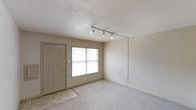 This 2-bedroom, 1-bathroom unit is thoughtfully laid out across a single floor, making efficient use of its space to deliver a comfortable and functional living environment. The living area greets residents at the entry, featuring soft wall-to-wall carpeting that adds warmth underfoot, while a large window allows natural light to fill the room throughout the day. A track lighting fixture mounted on the ceiling provides additional illumination and a modern touch against the textured popcorn ceiling. The entryway is finished with tile flooring, offering a durable and practical transition zone from the outdoors. Neutral wall tones throughout the unit create a clean, versatile backdrop well-suited to a variety of décor styles. The two bedrooms offer comfortable personal retreats, while the single bathroom serves the needs of the household. The overall layout is straightforward and accessible, ideal for individuals, couples, or small families seeking a well-appointed living space. The unit's design prioritizes functionality and ease of living, with each area connected in a logical and convenient flow that maximizes the usability of the available square footage.