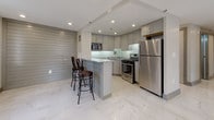 This well-appointed two-bedroom, two-bathroom unit showcases a thoughtfully designed single-floor layout with a clean, contemporary aesthetic throughout. The living area features light wood-style flooring, recessed lighting, and a large window framing urban city views, creating a bright and open atmosphere.

The kitchen is a standout space, outfitted with grey cabinetry, granite countertops, a glass tile backsplash, and a full suite of stainless steel appliances including a gas range, built-in microwave, dishwasher, and refrigerator. A peninsula with bar seating and a textured shiplap-style accent wall adds character and functionality. Polished marble-style porcelain tile floors extend through the kitchen and into the spacious main living area, which also benefits from city-facing windows and recessed lighting.

Both bedrooms offer wood-style flooring, recessed lighting, and neutral walls. One bedroom includes a double closet with paneled doors, providing ample storage. The two bathrooms are finished with marble-style wall and floor tiles, soaking tubs, mosaic tile accent borders, and contemporary vanities, delivering a spa-like quality. The overall design is cohesive, modern, and well-finished throughout.