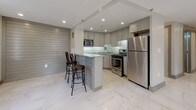 This well-appointed two-bedroom, two-bathroom unit showcases a thoughtfully designed single-floor layout with a clean, contemporary aesthetic throughout. The living area features light wood-style flooring, recessed lighting, and a large window framing urban city views, creating a bright and open atmosphere.

The kitchen is a standout space, outfitted with grey cabinetry, granite countertops, a glass tile backsplash, and a full suite of stainless steel appliances including a gas range, built-in microwave, dishwasher, and refrigerator. A peninsula with bar seating and a textured shiplap-style accent wall adds character and functionality. Polished marble-style porcelain tile floors extend through the kitchen and into the spacious main living area, which also benefits from city-facing windows and recessed lighting.

Both bedrooms offer wood-style flooring, recessed lighting, and neutral walls. One bedroom includes a double closet with paneled doors, providing ample storage. The two bathrooms are finished with marble-style wall and floor tiles, soaking tubs, mosaic tile accent borders, and contemporary vanities, delivering a spa-like quality. The overall design is cohesive, modern, and well-finished throughout.