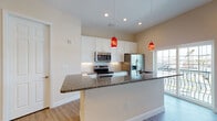 Located at 5500 Main St in New Port Richey, Pasco County, Florida, this two-story residence offers a well-designed layout with modern finishes throughout. The open-concept main living area features light wood-style flooring that extends seamlessly through the living and dining spaces, complemented by recessed lighting and a decorative chandelier that add warmth and brightness to the generous room proportions.

The kitchen is a standout feature, showcasing white shaker-style cabinetry, granite countertops, a tile backsplash, and a full suite of stainless steel appliances including a refrigerator with ice maker, electric range, and microwave. A large peninsula with pendant lighting in bold red accents provides additional prep and seating space. A sliding glass door leads directly to a private balcony, offering outdoor views of the surrounding area.

A half bath on the main level includes a pedestal sink and tile flooring, providing convenience for guests. Upstairs, the bedrooms feature plush carpeting and curved architectural wall details. The upper-level bathroom includes a soaking tub with white subway tile surround and a mosaic tile accent border. A dedicated laundry area with side-by-side washer and dryer and built-in shelving adds practical functionality to this well-appointed home.