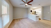 Located at 29 Dansey Cir in Durham, NC, this single-floor, one-bedroom, one-bathroom residence offers a well-designed layout that maximizes its comfortable footprint. The open-concept living and kitchen area serves as the heart of the home, where soft carpet transitions into durable hardwood-style flooring in the kitchen. The kitchen is equipped with stainless steel appliances, including a refrigerator and dishwasher, crisp white cabinetry, a clean white countertop peninsula, and a single-basin sink — all thoughtfully arranged for efficient use of space. A ceiling fan overhead adds to the airy feel of the living area, which also features direct access to a private wooden balcony overlooking a lush, tree-lined backdrop — a serene outdoor retreat. The spacious bedroom offers plush carpeting, a ceiling fan, ample closet space, and large windows that invite natural light and greenery views. The full bathroom features a clean, modern aesthetic with white cabinetry, a white countertop vanity with undermount sink, and a full tub/shower combination, all accented by warm wood-tone flooring. Neutral tones and textured ceilings carry throughout, creating a cohesive and tranquil atmosphere across the entire residence.