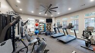 Located at 7805 S Union Ave in Tulsa, Oklahoma, this fitness center offers a comprehensive, single-floor exercise space designed to support a wide range of workout routines. The room is bright and inviting, with multiple windows along the walls that allow abundant natural light to fill the space, complemented by recessed ceiling lighting and a large ceiling fan that promotes air circulation during workouts.

The layout is thoughtfully organized to accommodate both cardio and strength training. A row of treadmills and an elliptical machine lines one side of the room, providing dedicated space for cardiovascular exercise. On the opposite side, a multi-station cable and weight machine offers versatile strength training options. A full rack of dumbbells is neatly arranged for free weight exercises, alongside a TAC-branded rack stocked with kettlebells, medicine balls, and stability balls of varying sizes to support functional fitness training.

Floor-to-ceiling mirrors span one wall, enhancing the sense of space and allowing users to monitor their form. Wall-mounted flat-screen televisions provide entertainment during workouts. Durable rubber flooring covers the exercise area, ensuring safety and comfort. Rustic wooden shelving adds a decorative touch, and a water station is conveniently available. The entrance features a glass-paneled door, maintaining an open and welcoming atmosphere throughout this well-appointed fitness facility.