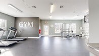 Located at 708 Glamorgan Way in Rock Hill, South Carolina, this single-floor community fitness center offers a well-appointed and thoughtfully organized workout space. The gym features a clean, modern aesthetic with light sage-green walls, a bold accent wall bearing the "GYM" signage, and durable speckled rubber flooring designed to withstand heavy use.

Natural light pours in through multiple windows fitted with blinds, creating a bright and welcoming environment throughout the space. Overhead fluorescent lighting supplements the natural light, ensuring excellent visibility at all times.

The facility is comprehensively equipped for a full-body workout experience. Cardio options include multiple treadmills, while the strength training area features a multi-function cable machine, a power rack with a weight bench, a full dumbbell rack, medicine ball storage, and a wall-mounted mirror to assist with form. A mounted flat-screen television adds an entertainment element to the workout experience. Additional accessories such as exercise mats and a variety of weighted implements are also available.

A glass-panel exterior door provides convenient access and contributes to the open, airy feel of the space. The overall design is functional, clean, and modern, making this gym a practical and inviting facility for residents seeking a convenient on-site fitness option.