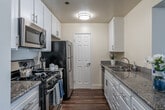 Located at 15555 Huntington Village Lane in Huntington Beach, CA, this well-appointed single-floor home offers a comfortable and functional layout across two bedrooms and two closets. The open living room is a standout feature, showcasing rich hardwood flooring, a classic fireplace with a white mantel, a ceiling fan, and large sliding glass doors with vertical blinds that fill the space with natural light and provide outdoor access. Plantation shutters on additional windows add a refined touch to the living area. The galley-style kitchen is thoughtfully designed with white shaker cabinetry, granite countertops, a stainless steel sink, and a full suite of stainless steel appliances including a gas range, microwave, and refrigerator. Hardwood flooring continues throughout the kitchen, which connects seamlessly to the living area. Both bedrooms are carpeted for comfort and finished with neutral taupe walls. The spacious primary bedroom includes access to a well-organized walk-in closet with built-in shelving and hanging rods. The second bedroom also features a closet and sliding door access. A wall-mounted mini-split unit provides efficient climate control. The textured ceilings and clean white trim throughout lend a cohesive, move-in-ready aesthetic to this Huntington Beach home.