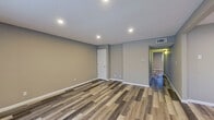 This single-floor space presents a clean, modern aesthetic defined by warm neutral tones and consistent wood-look vinyl plank flooring that runs throughout every room. The open living area is bright and generously proportioned, featuring recessed lighting embedded in a textured ceiling and a large sliding window that invites natural light and outdoor views. White baseboards provide a crisp contrast to the soft gray-taupe walls, lending the space a fresh, contemporary feel.

The kitchen is well-equipped and thoughtfully designed, showcasing white shaker-style cabinetry, speckled granite countertops, and stainless steel appliances including a full-size refrigerator and electric range. The layout maximizes available counter and storage space efficiently.

The bedrooms are comfortably sized, each featuring the same vinyl plank flooring, neutral wall tones, and windows with blinds that allow for natural light while maintaining privacy. A dedicated closet space offers built-in shelving and a hanging rod for organized storage.

The bathroom is outfitted with a full-size soaking tub and shower combination, surrounded by clean white surround panels with built-in recessed shelving. White cabinetry and chrome fixtures complete the tidy, functional design. Overall, the space delivers a cohesive, move-in-ready environment with modern finishes throughout.