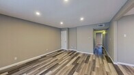 This single-floor space presents a clean, modern aesthetic defined by warm neutral tones and consistent wood-look vinyl plank flooring that runs throughout every room. The open living area is bright and generously proportioned, featuring recessed lighting embedded in a textured ceiling and a large sliding window that invites natural light and outdoor views. White baseboards provide a crisp contrast to the soft gray-taupe walls, lending the space a fresh, contemporary feel.

The kitchen is well-equipped and thoughtfully designed, showcasing white shaker-style cabinetry, speckled granite countertops, and stainless steel appliances including a full-size refrigerator and electric range. The layout maximizes available counter and storage space efficiently.

The bedrooms are comfortably sized, each featuring the same vinyl plank flooring, neutral wall tones, and windows with blinds that allow for natural light while maintaining privacy. A dedicated closet space offers built-in shelving and a hanging rod for organized storage.

The bathroom is outfitted with a full-size soaking tub and shower combination, surrounded by clean white surround panels with built-in recessed shelving. White cabinetry and chrome fixtures complete the tidy, functional design. Overall, the space delivers a cohesive, move-in-ready environment with modern finishes throughout.
