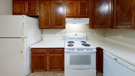Located at 45 East St in Victor, NY, this single-floor unit offers a straightforward, functional layout designed for comfortable everyday living. The floor plan, visible from an overhead view, reveals a well-organized arrangement of living, kitchen, and bedroom spaces connected by a practical entryway with tile flooring.

The living area is generously sized, featuring neutral beige walls, wall-to-wall carpeting, and a textured ceiling. A sliding glass door leads to a private balcony, allowing natural light to fill the room and providing outdoor views. A wall-mounted air conditioning unit and baseboard heating ensure year-round climate control.

The kitchen is equipped with rich, warm-toned oak cabinetry providing ample storage, white countertops, and a full suite of white appliances including a GE electric range with overhead ventilation, refrigerator, and dishwasher. A window above the sink adds natural light, and durable tile flooring runs throughout.

Two carpeted bedrooms each feature neutral walls, window blinds for privacy, and baseboard heating. Both rooms offer a calm, understated ambiance well-suited for rest.

The bathroom includes a full-size soaking tub and shower combination with a molded surround and chrome fixtures, maintaining a clean and practical design throughout.