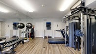 Located at 111 Cheswick Cir in Yorktown, Virginia, this fitness center is a compact yet comprehensively outfitted exercise facility designed to support a full range of workout routines. The single-room space features durable wood-style plank flooring throughout, providing a clean and modern aesthetic that complements its neutral gray and white walls.

The room is well-lit by overhead fluorescent fixtures and benefits from natural light via a glass-paneled entry door, which also provides a view of the surrounding greenery outside. Large wall-mounted mirrors along one side of the room visually expand the space and allow users to monitor their form during workouts.

The facility is stocked with a diverse selection of equipment. Cardio options include a treadmill, an elliptical trainer, and a stationary bike. For strength training, the room houses a multi-function cable machine, a selectorized strength unit, and a weight bench. A full rack of dumbbells, kettlebells of varying weights, stability balls, and wall-mounted foam rollers round out the free weights and functional training offerings.

Additional amenities include a restroom accessible directly from the fitness floor, wall-mounted equipment storage, and a fire safety system. The space is thoughtfully arranged to maximize usability, making it a practical and functional destination for residents seeking a convenient on-site workout facility.