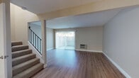 Located at 41716 Gifford St in Fremont, California, this two-story home offers a well-organized layout across both levels. The main floor features an open living area finished with durable hardwood-style flooring and a textured ceiling. A large sliding glass door fitted with vertical blinds fills the space with natural light and provides access to the outdoors, while a wall-mounted HVAC unit ensures year-round comfort. A staircase with a sleek black metal railing connects the two floors. The kitchen is thoughtfully appointed with white shaker cabinetry, dark granite-style countertops, a stainless steel dishwasher, a full-size refrigerator, and a single-basin sink — all complemented by light hardwood-style flooring and a window that brings in additional natural light. Upstairs, the bedrooms are carpeted and feature ceiling fans and windows with vertical blinds. The bathroom is outfitted with a white vanity, dark stone countertop, a large mirror, and hardwood-style flooring, with a separate shower and adjacent closet space. The detached garage features a vaulted wood-beam ceiling and an automatic opener, offering generous storage potential. Throughout, the home presents a clean, updated aesthetic with neutral tones.