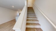 Located at 101 N 7th Ave in Cornelius, Oregon, this two-bedroom, two-bathroom unit is thoughtfully laid out across two floors. The main level opens into a bright living room with light hardwood-style flooring, recessed lighting, a front-facing window that brings in natural light, and a wall-mounted HVAC unit. A staircase along the living area leads to the upper floor. The kitchen is a standout feature, showcasing crisp white shaker cabinetry, a marble-look countertop island, subway tile backsplash, and a full suite of stainless steel appliances including a refrigerator, dishwasher, range, and microwave. A second bedroom on the main level features matching hardwood-style flooring and a window. The main-level bathroom offers a marble-look vanity top, tile flooring, and accessibility grab bars. Upstairs, both bedrooms are carpeted and equipped with ceiling fans. The primary bedroom includes a sliding-door closet and a wall vent. The upper-level bathroom features a glass-enclosed walk-in shower, a marble-look vanity, subway tile accents, and hardwood-style flooring. Clean white walls and recessed lighting throughout lend the space a cohesive, modern aesthetic.