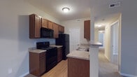 Located at 4460 Mountain Laurel Rd in Hilliard, Ohio, this single-floor residence offers a well-organized and functional layout designed for comfortable everyday living. The kitchen is a standout feature, outfitted with rich warm-toned wood cabinetry that provides generous storage space above and below the countertops. Black appliances — including an electric range, over-the-range microwave, and refrigerator — give the kitchen a cohesive, practical aesthetic. The laminate countertops offer ample prep space, and a peninsula with a built-in sink and breakfast bar creates a natural transition between the kitchen and the adjoining living areas. The kitchen features durable hardwood-style flooring, while the hallway and adjacent rooms transition to plush carpeting, adding warmth and comfort throughout. A textured ceiling and flush-mount lighting fixtures provide consistent illumination across the space. A paneled interior door leads from the kitchen to additional areas of the home, and the open hallway beyond hints at well-connected, easy-to-navigate floor plan. Overall, the residence presents a clean, move-in ready environment with a neutral color palette suited to a variety of interior styles.