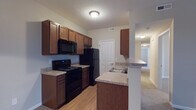 Located at 4460 Mountain Laurel Rd in Hilliard, Ohio, this single-floor residence offers a well-organized and functional layout designed for comfortable everyday living. The kitchen is a standout feature, outfitted with rich warm-toned wood cabinetry that provides generous storage space above and below the countertops. Black appliances — including an electric range, over-the-range microwave, and refrigerator — give the kitchen a cohesive, practical aesthetic. The laminate countertops offer ample prep space, and a peninsula with a built-in sink and breakfast bar creates a natural transition between the kitchen and the adjoining living areas. The kitchen features durable hardwood-style flooring, while the hallway and adjacent rooms transition to plush carpeting, adding warmth and comfort throughout. A textured ceiling and flush-mount lighting fixtures provide consistent illumination across the space. A paneled interior door leads from the kitchen to additional areas of the home, and the open hallway beyond hints at well-connected, easy-to-navigate floor plan. Overall, the residence presents a clean, move-in ready environment with a neutral color palette suited to a variety of interior styles.