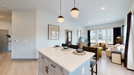 This well-appointed 2-bedroom, 2-bathroom residence offers a thoughtfully designed single-level layout with a clean, modern aesthetic. The open-concept kitchen and living area serves as the heart of the home, featuring white shaker cabinetry, stainless steel appliances, and a central island with a quartz countertop illuminated by a pair of globe pendant lights — ideal for casual dining and entertaining. Light wood-toned flooring flows seamlessly throughout, lending a bright and cohesive feel to the entire space. The living room is bathed in natural light from expansive windows dressed with blinds and dark accent curtains, creating a welcoming and airy atmosphere. The primary bedroom is a generously sized retreat with high ceilings, a private ensuite bathroom, and direct closet access. The second bedroom offers comfortable proportions with its own closet for ample storage. Both bathrooms are finished in a clean, neutral palette, with one featuring a tub-shower combination with subway tile surround and light wood-toned flooring. Walk-in closets with built-in shelving and hanging systems provide practical storage solutions. Throughout the residence, light-toned walls and recessed lighting reinforce the modern, open character of the space.