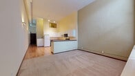Located at 322 Euclid Ave in Cleveland, OH, this two-floor unit offers a thoughtful layout that blends architectural character with practical living spaces. The main level features a generously proportioned living area with soaring ceilings and neutral-toned carpet, complemented by tall windows that invite natural light and views of the surrounding urban streetscape. An arched doorway adds a distinctive architectural detail, lending a sense of historic charm to the open layout.

The kitchen is well-equipped with white cabinetry extending to considerable height, laminate countertops, hardwood flooring, and a full suite of appliances including a refrigerator, electric range, microwave, and dishwasher. A raised breakfast bar separates the kitchen from the main living space, providing both functionality and definition between areas.

The bathroom features tile flooring, a tub-shower combination, a vanity with under-cabinet storage, a mirrored medicine cabinet, and wood flooring extending into the vanity area. Additional rooms offer carpeted floors, neutral walls, and ample natural light, with one room featuring a closet. The second floor expands the living footprint, providing flexible space suited to a variety of uses throughout the unit.