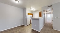 This single-story residence offers a well-organized layout across two bedrooms, two bathrooms, a combined kitchen and living area, a hallway, and two closets. The open-concept living room features neutral-toned carpet, a ceiling fan with light fixture, and a large window alongside a glass-panel exterior door that invites natural light into the space. The kitchen is defined by a peninsula-style breakfast bar that separates it from the living area, warm-toned wood cabinetry, light countertops, wood-look vinyl flooring, and white appliances including a refrigerator, stove, microwave, and dishwasher. A secondary door in the kitchen provides additional exterior access.

Both bedrooms are carpeted and equipped with ceiling fans. The primary bedroom features two windows that bring in ample natural light, while the secondary bedroom includes a single window. Each room has access to its own closet. The two bathrooms maintain a consistent design aesthetic; one includes a tub-shower combination with full white tile surround, while the other features wood-look flooring, a wood-cabinet vanity with a light countertop, a large mirror, and a tub-shower area. The hallway connects the bedrooms and bathrooms, creating a cohesive and functional flow throughout the residence.