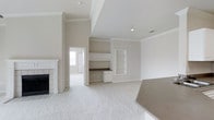 This well-appointed single-floor residence offers 2 bedrooms and 2 bathrooms thoughtfully arranged within a generous and open floor plan. The main living area is bright and airy, finished with plush wall-to-wall carpeting and neutral tones throughout, creating a clean and welcoming atmosphere. Crown molding adds a refined architectural touch, while recessed lighting enhances the sense of openness.

A standout feature of the living space is the built-in desk nook, complete with overhead shelving and cabinetry — ideal for a home office or study area. Adjacent to it, a set of built-in display shelves provides additional storage and aesthetic character. A classic fireplace with a white surround anchors one side of the room, offering a cozy focal point.

The open sightlines connect the living area seamlessly to the kitchen, where a countertop is partially visible, suggesting a functional and accessible layout. A doorway leads to additional rooms, maintaining a smooth flow throughout the home. The light, neutral color palette — consistent across walls, trim, and flooring — gives the entire space a cohesive, move-in-ready appeal suited for a variety of lifestyles.