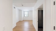 Located at 101 W 10th St in downtown Wilmington, Delaware, this 2-bedroom, 1-bathroom unit offers a clean, modern aesthetic throughout its efficiently designed single-floor layout. Warm honey-toned hardwood-style flooring flows consistently across all rooms, providing a cohesive and inviting atmosphere.

The combined kitchen and living area serves as the heart of the unit. The kitchen is outfitted with sleek, flat-front charcoal cabinetry extending to the ceiling for ample storage, complemented by matching dark countertops, a textured tile backsplash, and a full suite of stainless steel appliances including an electric range with overhead microwave.

The spacious primary bedroom offers generous room for furnishings, with recessed lighting, a large sliding closet with panel doors, and a window overlooking the surrounding urban streetscape. The second bedroom is equally well-appointed, featuring a window with horizontal blinds that frames views of neighboring city buildings, filling the room with natural light.

A connecting hallway leads to the full bathroom, which includes a soaking tub with shower combination, brushed gold fixtures, a curved shower rod, and clean white tile surround. Throughout the unit, crisp white walls, recessed lighting, and contemporary finishes create a bright, minimal, and functional living environment.