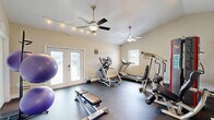 Located in Tampa, FL, this dedicated exercise room is a fully functional fitness space designed to support a comprehensive workout routine. The room features vaulted ceilings that lend an open, airy feel, complemented by two ceiling fans that promote air circulation during workouts. Track lighting along the ceiling provides bright, even illumination throughout the space.

The durable dark flooring is well-suited for gym use, offering both resilience and easy maintenance. Natural light filters in through multiple windows and a set of glass French doors, which also provide views of and access to an outdoor area, believed to be a pool. This connection to the outdoors enhances the overall ambiance of the room.

The space is outfitted with a diverse range of fitness equipment, including a treadmill, elliptical trainer, multi-station cable machine, a SportsArt-brand cable system, adjustable weight bench, a full dumbbell rack, and multiple stability balls on a dedicated stand. Storage doors along one wall offer organizational convenience.

The walls are finished in a neutral warm beige tone, creating a clean and motivating environment. Overall, this exercise room is thoughtfully designed to provide a private, fully equipped fitness experience within a comfortable and well-lit setting.