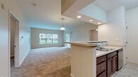 Located at 830 Holt Rd in Webster, NY, this single-floor residence offers two bedrooms and two bathrooms within a well-organized and functional layout. The combined kitchen and living room serves as the heart of the home, with the kitchen featuring rich dark wood cabinetry, stainless steel appliances including a full-size refrigerator, microwave, and range, and durable tile flooring. The adjacent living area provides a comfortable open space with natural light and direct access to a private balcony through a sliding glass door, offering pleasant outdoor views. Both bedrooms are carpeted and equipped with ceiling fans, with windows that bring in ample natural light and views of the surrounding greenery. The spacious primary bedroom includes generous wall space for flexible furniture arrangements. The two bathrooms are finished with tile flooring and include accessibility features such as grab bars. The first bathroom offers a shower-tub combo, while the second features a standalone walk-in shower and a dark wood vanity with a white countertop. A dedicated hallway and closet provide additional storage and organizational convenience throughout the home.