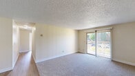 Located in Vancouver, WA, this single-floor, 2-bedroom, 2-bathroom residence offers a practical and comfortable layout. The combined living and dining area is bright and open, featuring plush carpeting, neutral walls, and a textured ceiling. A sliding glass door fills the space with natural light and provides direct access to a private balcony with outdoor views of surrounding greenery. The kitchen is well-equipped with dark espresso cabinetry, light countertops, wood-look vinyl flooring, and a full suite of appliances including a refrigerator and dishwasher. A hallway connects the main living spaces to the bedrooms and bathrooms, with wood-look flooring continuing through the corridor. The spacious primary bedroom includes a closet and baseboard heating, while the second bedroom benefits from a large window that brings in generous natural light. Both bedrooms are carpeted and feature ample closet space — with five closets total throughout the unit. The two bathrooms are finished with dark cabinetry, wide vanity counters, and wood-look flooring. A dedicated utility room and additional in-unit storage round out this well-organized and functional floor plan.