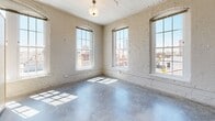 Located at 131 Wayne Ave in Dayton, Ohio, this single-floor unit showcases a compelling mix of historic industrial architecture and contemporary finishes. Throughout the space, polished concrete floors provide a sleek, durable foundation that complements the whitewashed exposed brick walls found in several rooms. Large, arched and multi-pane windows are a defining architectural feature, flooding the interior with generous natural light and offering views of the surrounding Dayton streetscape.

The open kitchen is equipped with white cabinetry, a center island with a light countertop, black appliances including a range, microwave, refrigerator, and dishwasher, and is positioned adjacent to oversized windows that enhance the bright, airy atmosphere. Exposed ductwork and track lighting along the ceiling contribute to the unit's industrial aesthetic.

Additional rooms include a private bedroom with a ceiling fan, painted brick walls, and concrete floors, as well as a well-lit living area with prominent arched windows and built-in shelving. The bathroom features a walk-in shower, vanity with storage, and polished concrete flooring. A corridor connects the spaces efficiently, reinforcing the unit's cohesive, loft-inspired character.