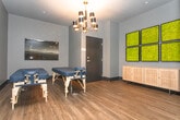Located at 5251 Peachtree Industrial Blvd in Chamblee, Georgia, this single-floor wellness studio is designed with a calming, sophisticated aesthetic that sets the tone for a restorative experience. Throughout the space, warm wood-toned flooring contrasts beautifully against deep charcoal-gray walls and bold dark baseboards, creating an atmosphere that feels both grounded and refined.

A standout decorative feature found across multiple rooms is a collection of framed preserved moss wall panels, arranged in grid formations above a natural rattan-front credenza. These biophilic accents introduce organic texture and vibrant green tones that enliven the otherwise moody interior palette.

The treatment rooms are spacious and purposefully appointed, each featuring massage tables positioned beneath striking mid-century modern chandeliers with brass accents and cylindrical black shades. Carefully considered lighting adds warmth while maintaining a tranquil, low-key ambiance suited to therapeutic services.

Additional rooms in the suite provide flexible utility space, with clean walls, black-framed doorways with brass hardware, and consistent wood flooring that unifies the layout. The interior design balances dark, moody tones with natural materials, resulting in a cohesive and professional environment. This space is well-suited for massage therapy, wellness services, or similar health-focused practices.