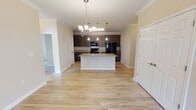Located at 7135 Brandy Run Dr in Mechanicsville, Virginia, this single-floor residence offers a well-designed open-concept layout that seamlessly connects the kitchen, dining, and living areas. The kitchen is a standout feature, boasting dark espresso cabinetry that extends to the ceiling, granite countertops, a large central island with a built-in sink and pendant lighting overhead, and a full suite of black appliances including a range, microwave, and refrigerator. Crown molding accents the kitchen and main living areas, adding a refined architectural touch throughout. Light wood-style flooring flows across the main living spaces, complementing the warm neutral tones of the walls. The living and dining areas are enhanced by elegant chandelier and ceiling fan fixtures, with large windows and glass doors drawing in abundant natural light. Carpeted bedrooms offer a comfortable retreat, each featuring windows with outdoor views and ceiling fans for year-round comfort. The primary bathroom is generously proportioned, featuring a dual-sink vanity with granite countertops, dark wood cabinetry, a large mirror, built-in shelving, and light wood-style flooring. A second full bathroom includes a tub-shower combination with clean white tile surround and a granite vanity. Completing the home is a dedicated laundry area with a stacked washer and dryer unit.