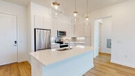 Located at 1 Riverside Ave in Jacksonville, FL, this thoughtfully designed 2-bedroom, 2-bathroom residence offers a bright and modern living experience across a single level. The open-concept layout seamlessly connects the kitchen, dining, and living areas into one expansive, light-filled space. The kitchen is a standout feature, showcasing sleek white cabinetry extending to the ceiling, a large center island with a white quartz countertop and undermount sink, stainless steel appliances, and a classic subway tile backsplash. Globe pendant lights add a stylish focal point overhead. Light-toned hardwood flooring flows throughout the entire residence, enhancing the clean, contemporary aesthetic. The living area benefits from large windows and a glass door that opens to a private balcony, filling the room with natural light. Both bedrooms are generously proportioned, with ceiling fans, wide windows, and ample closet space—including a spacious walk-in closet with built-in wire shelving. The bathrooms feature crisp white tile surrounds with tub-shower combinations and wood-look flooring. Additional conveniences include a dedicated laundry area and a hallway connecting all spaces efficiently. The overall ambiance is bright, clean, and move-in ready.