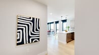 This thoughtfully designed single-floor residence showcases a seamless blend of modern aesthetics and functional living. Light hardwood flooring flows throughout the open-concept main area, connecting the kitchen and living room in a cohesive, airy layout.

The kitchen is a standout feature, outfitted with two-tone wood cabinetry in warm and light finishes, a striking hexagonal mosaic tile backsplash, stainless steel appliances, and a generous white quartz peninsula with seating for multiple guests. Pendant lighting above the peninsula adds a polished, contemporary touch.

The living area is bathed in natural light through a wall of large, floor-to-ceiling windows fitted with sleek black roller shades, offering expansive city views that serve as a dynamic backdrop to the space.

Both bedrooms are comfortably proportioned, featuring the same light hardwood flooring, large windows with urban vistas, and clean white walls that create a calm, restful atmosphere.

The bathrooms are finished with dark large-format floor tiles, floating wood-toned vanities, white quartz countertops, and subway-tiled walls in both the walk-in shower and soaking tub configurations. A circular mirror in each bathroom adds a refined, modern detail.

Throughout the space, the interplay of natural textures, neutral tones, and contemporary finishes creates a polished yet welcoming environment.