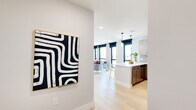 This thoughtfully designed single-floor residence showcases a seamless blend of modern aesthetics and functional living. Light hardwood flooring flows throughout the open-concept main area, connecting the kitchen and living room in a cohesive, airy layout.

The kitchen is a standout feature, outfitted with two-tone wood cabinetry in warm and light finishes, a striking hexagonal mosaic tile backsplash, stainless steel appliances, and a generous white quartz peninsula with seating for multiple guests. Pendant lighting above the peninsula adds a polished, contemporary touch.

The living area is bathed in natural light through a wall of large, floor-to-ceiling windows fitted with sleek black roller shades, offering expansive city views that serve as a dynamic backdrop to the space.

Both bedrooms are comfortably proportioned, featuring the same light hardwood flooring, large windows with urban vistas, and clean white walls that create a calm, restful atmosphere.

The bathrooms are finished with dark large-format floor tiles, floating wood-toned vanities, white quartz countertops, and subway-tiled walls in both the walk-in shower and soaking tub configurations. A circular mirror in each bathroom adds a refined, modern detail.

Throughout the space, the interplay of natural textures, neutral tones, and contemporary finishes creates a polished yet welcoming environment.