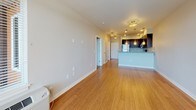 This single-floor residence presents a thoughtfully designed open-concept layout with a neutral color palette and warm hardwood flooring throughout the main living areas. The spacious living room benefits from large windows fitted with horizontal blinds, allowing ample natural light to filter in while offering views of the surrounding outdoors. The open layout flows seamlessly toward the kitchen and dining area, creating a connected and functional living space.

The kitchen is well-equipped and features dark espresso cabinetry, stainless steel appliances including a refrigerator, range, and microwave, and granite countertops with a subtle penny-tile backsplash. Pendant lighting above the counter and recessed ceiling lights add both style and practicality to the space.

The bedroom is carpeted for comfort and includes a ceiling fan with integrated lighting and a window that invites natural light. The bathroom is finished with a dark-cabineted vanity topped with granite countertops, an undermount sink, and a large mirror, complemented by tile wall surrounds. Clean lines and neutral tones throughout contribute to the unit's cohesive, modern aesthetic.