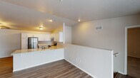 This single-story space is designed with a clean, contemporary aesthetic and a practical open layout. The kitchen serves as a central highlight, featuring white shaker-style cabinetry extending to the ceiling, light stone countertops with subtle veining, and a full suite of stainless steel appliances including a refrigerator, electric range, and over-the-range microwave. A peninsula with an integrated sink and generous counter overhang provides additional prep space and casual seating. Vaulted ceilings above the kitchen area add volume and visual interest to this zone.

The adjoining living area is finished with wood-look plank flooring and features a sliding glass door that opens to a balcony, allowing natural light to fill the space. A separate carpeted room, equipped with a ceiling fan and a window, offers a comfortable, quiet retreat. Two bathrooms are present, each finished with white cabinetry, light stone vanity tops, and wood-look flooring. One bathroom includes a walk-in shower, while the other offers a full vanity setup. A dedicated laundry area houses a full-size front-loading washer and dryer alongside wire shelving for added storage.