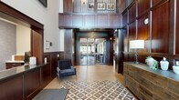 Located at 460 Wacouta St in Saint Paul, Minnesota, this thoughtfully designed communal space spans a single floor and comprises three distinct areas that together create a refined and welcoming environment. The grand lobby serves as the centerpiece, immediately impressing with its dramatic double-height ceilings, floor-to-ceiling dark mahogany wood paneling, and an upper-level mezzanine with decorative iron railings and framed artwork. Light hardwood flooring and a bold geometric-patterned area rug anchor the space, while a classic credenza with a table lamp and a sleek accent chair add curated furnishing touches. An abundance of natural light filters in through large glass entry doors and clerestory windows, enhancing the airy yet sophisticated atmosphere. Beyond the lobby, the lounge area offers a comfortable and versatile gathering space, featuring plush seating, a tiled fireplace flanked by built-in cabinetry with a wall-mounted television, and large windows that frame views of the surrounding streetscape. A dedicated social zone completes the layout, equipped with a high communal table, bar-height seating, a wet bar with pendant lighting, a textured accent wall, and a billiards table — making it an ideal space for both casual relaxation and social gatherings.
